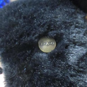 May include: Close-up of a black plush toy with a button that reads "F.A.O." and a tag that says "SCHWARZ". The toy has a soft, furry texture.