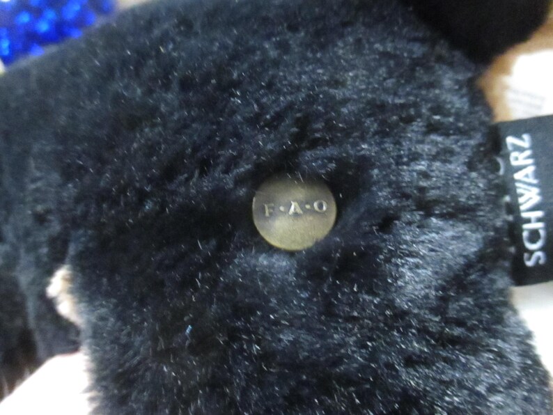 May include: Close-up of a black plush toy with a button that reads "F.A.O." and a tag that says "SCHWARZ". The toy has a soft, furry texture.