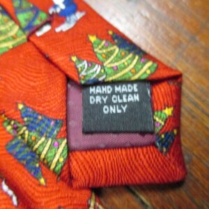 May include: Red Christmas tie with a repeating pattern of Christmas trees and Santa Claus figures. The tie has a label that reads "HAND MADE DRY CLEAN ONLY".