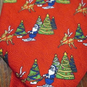 May include: Red Christmas tie with a repeating pattern of Santa Claus on skis, reindeer, and decorated Christmas trees. The tie has a textured surface and a festive holiday theme.