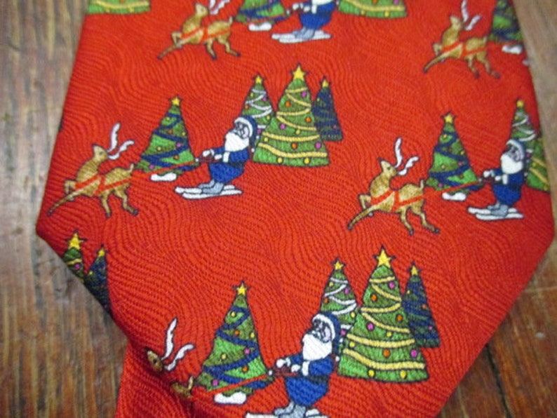 May include: Red Christmas tie with a repeating pattern of Santa Claus on skis, reindeer, and decorated Christmas trees. The tie has a textured surface and a festive holiday theme.