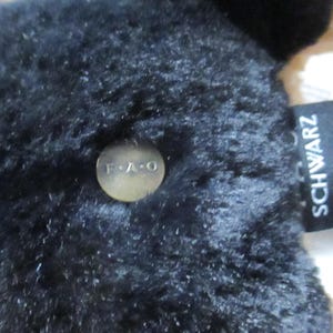 May include: Close-up of a black plush toy with a tag that reads "SCHWARZ". A small, round, gold-colored button with the letters "F.A.O" is attached to the plush toy. The toy has a soft, textured appearance.