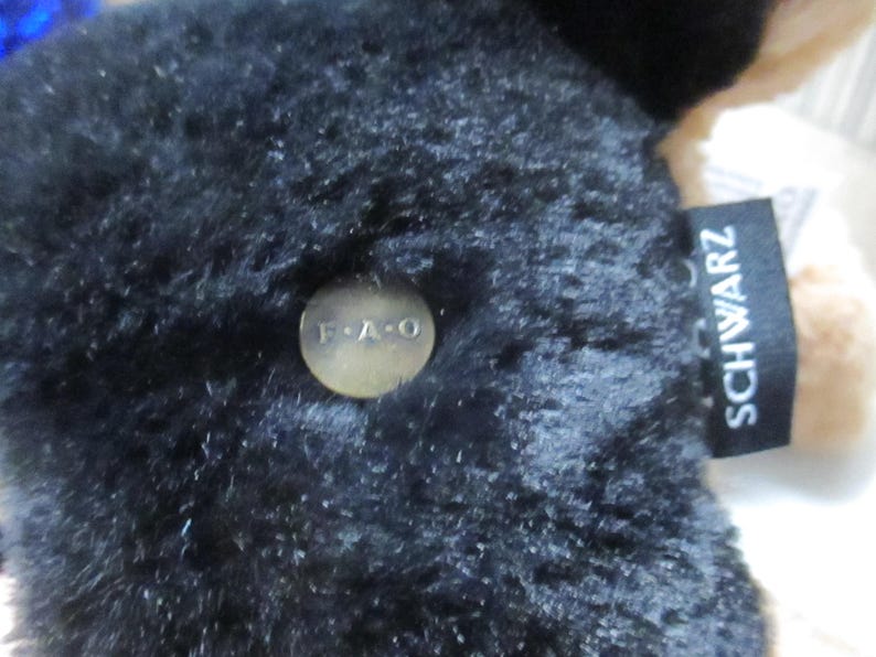 May include: Close-up of a black plush toy with a tag that reads "SCHWARZ". A small, round, gold-colored button with the letters "F.A.O" is attached to the plush toy. The toy has a soft, textured appearance.