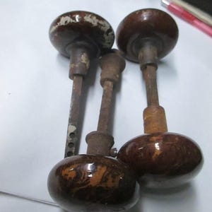 May include: A collection of vintage brown and white door knobs. The knobs have a rounded shape with a dark brown finish and a white, distressed top. The metal stems show signs of age and wear.