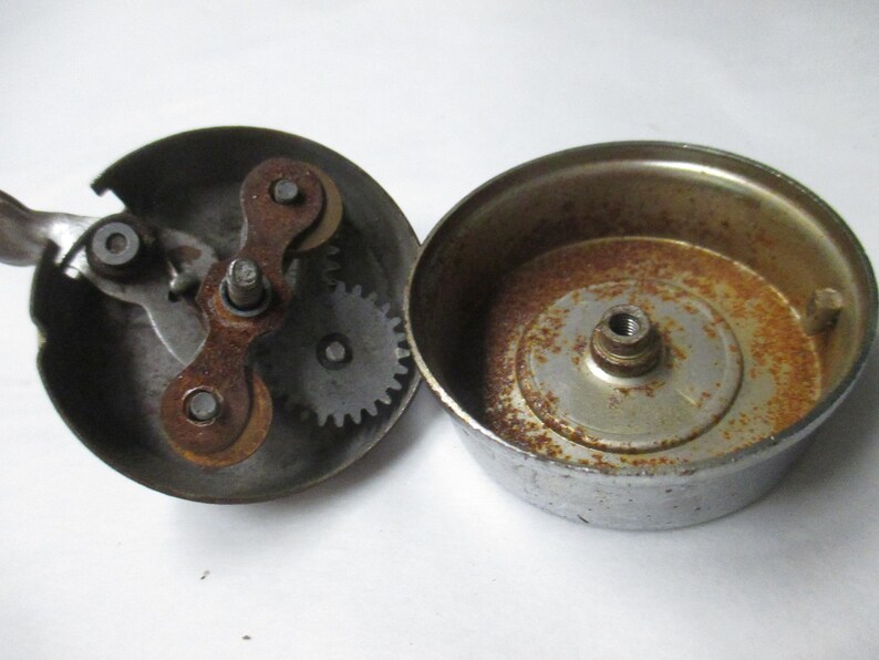 May include: A disassembled metal bicycle bell consisting of two circular components. One part features an internal gear mechanism with a lever, while the other is a hollow dome. Both pieces show visible signs of oxidation and rust on the metal.