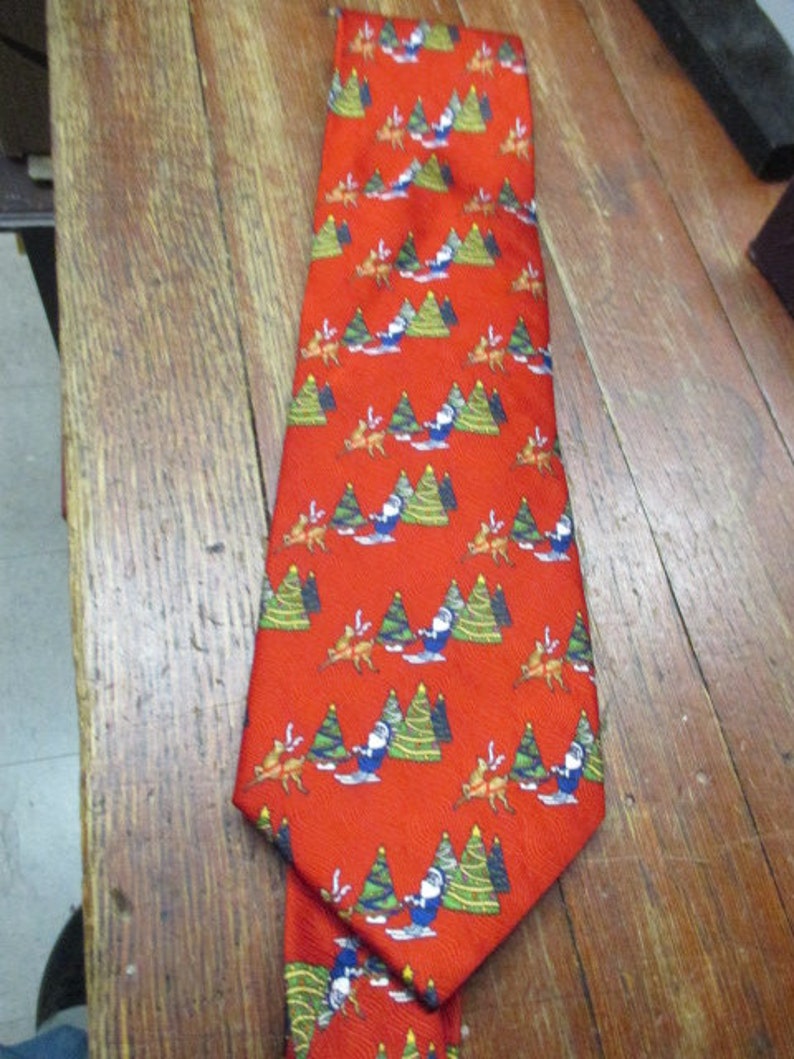 May include: Red Christmas-themed necktie with a repeating pattern of Santa Claus, reindeer, and Christmas trees. The tie is made of a smooth fabric and is suitable for festive occasions.