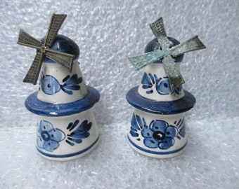 May include: Two ceramic windmill figurines. The windmills are white with blue floral designs and accents. Each has a dark blue top and a bronze-colored windmill blade. The base of each windmill is a light blue.