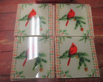 May include: Set of four glass coasters with a red cardinal bird on a green pine branch with red berries and pine cones. The coasters have a plaid border in red, green, and white.