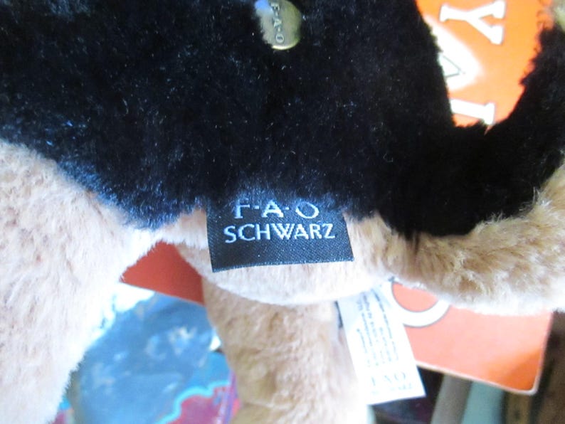 May include: Close-up of a plush toy with black fur on top and tan fur underneath. A black tag with the text "F.A.O. SCHWARZ" is attached. A gold-colored tag is also visible.