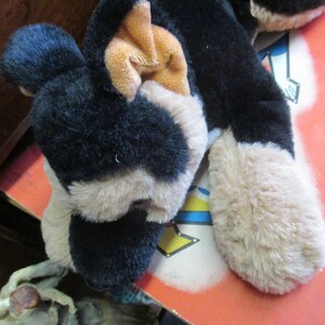 May include: A plush dog toy with black, tan, and white fur. The toy has floppy ears and a soft, cuddly appearance. The dog's paws are a light tan color. The toy is lying on a red surface.