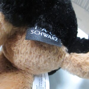 May include: A plush toy with black and tan fur. The toy has a tag that reads "F.A.O. SCHWARZ". The tag also includes the copyright information for the toy.