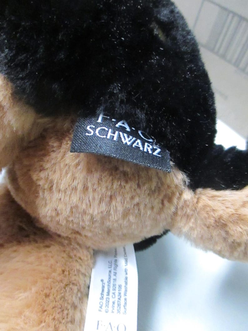 May include: A plush toy with black and tan fur. The toy has a tag that reads "F.A.O. SCHWARZ". The tag also includes the copyright information for the toy.