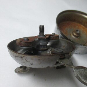 May include: A disassembled silver-toned metal bicycle bell with visible rust on the internal mechanism, central threaded screw, and lever. The bell housing is detached, revealing the inner components and a weathered, metallic finish throughout.