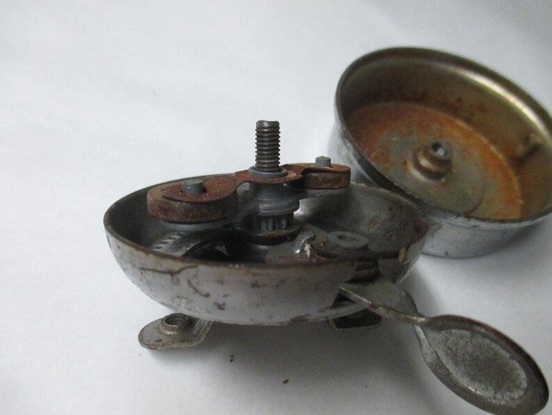 May include: A disassembled silver-toned metal bicycle bell with visible rust on the internal mechanism, central threaded screw, and lever. The bell housing is detached, revealing the inner components and a weathered, metallic finish throughout.
