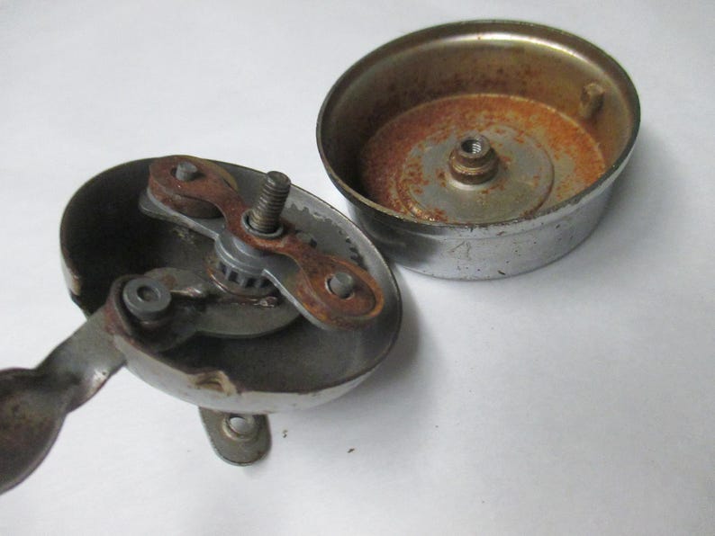 May include: A disassembled chrome bicycle bell consisting of two main parts. The base features an internal gear mechanism with a lever and visible rust. The separate circular top cover shows oxidation and rust on its interior surface.