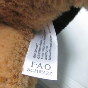 May include: Close-up of a plush toy with brown fur and a black patch. A white tag is attached, displaying the "FAO Schwarz" logo and washing instructions.