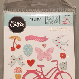 May include: A package of Sizzix Thinlits dies designed by Brenda Walton. The die-cuts include a pink bicycle, cherries, a butterfly, a heart, a bow, a polka dot banner, a swallow, and other decorative shapes. The package contains 14 dies.