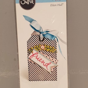 May include: Sizzix Thinlits die set by Eileen Hull. The package features a tag design with black and white stripes, a banner that says "friend", and a blue and white ribbon. The set includes 4 dies.