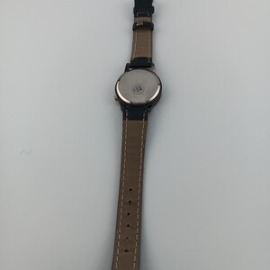 May include: A black wristwatch with a brown leather band. The watch face is round with a black bezel. The band is stitched with white thread and has several holes for adjustment.