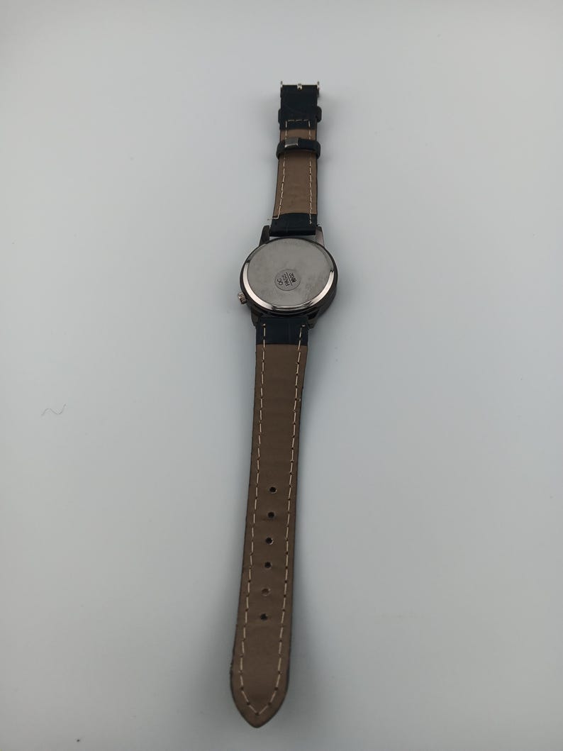 May include: A black wristwatch with a brown leather band. The watch face is round with a black bezel. The band is stitched with white thread and has several holes for adjustment.