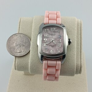 Puede incluir: Un reloj Activa Swiss plateado con una correa y esfera rosa claro. El reloj tiene una esfera rectangular con n&uacute;meros y agujas plateadas. Una moneda est&aacute; al lado del reloj para comparar el tama&ntilde;o.