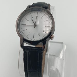 May include: A black wristwatch with a silver face and black leather band. The watch has a dark gray bezel and a small crown on the side. The watch face displays the numbers 1 through 12.