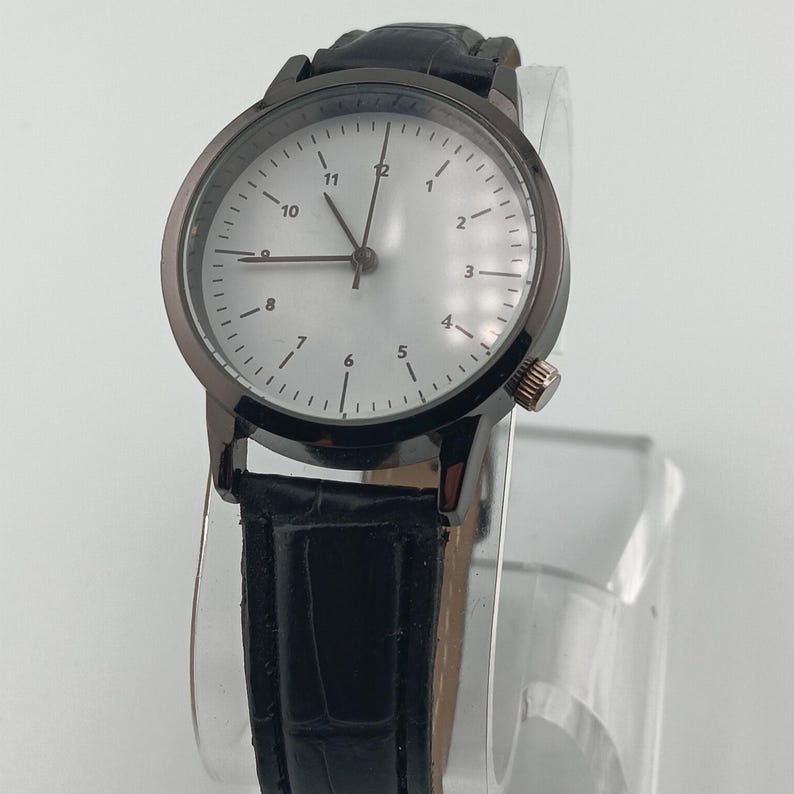 May include: A black wristwatch with a silver face and black leather band. The watch has a dark gray bezel and a small crown on the side. The watch face displays the numbers 1 through 12.