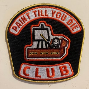 May include: A black and orange embroidered patch with the text "Paint Till You Die Club". The patch features a cartoon image of a person painting in a coffin.
