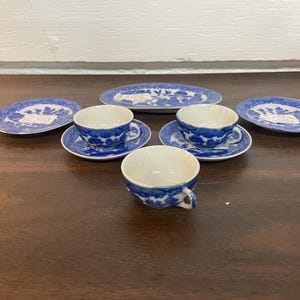 Può includere: Un set di tazze da tè, piattini e piatti da portata in porcellana blu e bianca. Le tazze e i piattini presentano un motivo floreale coordinato. I piatti da portata sono di forma ovale. Il set è disposto su una superficie di legno scuro.