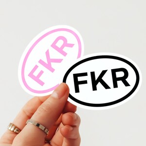 Puede incluir: Dos pegatinas ovaladas con las letras "FKR". Una pegatina tiene un borde rosa y letras rosas, la otra tiene un borde negro y letras negras. Las pegatinas se sostienen sobre un fondo blanco.