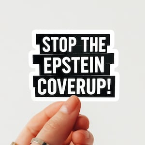 May include: A white sticker with black text that reads "STOP THE EPSTEIN COVERUP!". The sticker is held by a hand with a ring on the finger. The sticker has a white border.