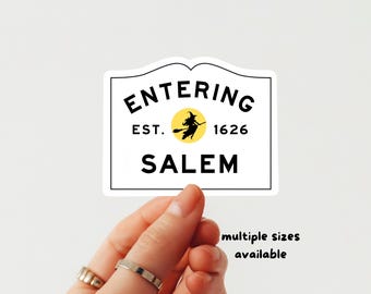 Puede incluir: Una pegatina rectangular blanca con borde negro que presenta el texto ENTERING SALEM y EST. 1626 en letras mayúsculas negras. Un círculo amarillo que contiene una silueta negra de una bruja volando en una escoba está centrado entre las fechas.