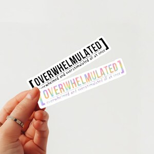 May include: Two stickers with the text "OVERWHELMULATED" in black text on a white background. The text is surrounded by brackets. The text is repeated on both stickers. The bottom sticker has a rainbow gradient effect.