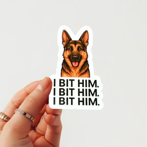 Puede incluir: Adhesivo con una ilustración de un perro pastor alemán y el texto "I BIT HIM. I BIT HIM. I BIT HIM." El perro tiene pelaje marrón y negro, una lengua rosa y un fondo blanco.
