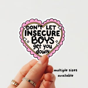 Könnte beinhalten: Ein herzförmiger Aufkleber mit einem gewellten rosa Rand und einer cremefarbenen Mitte. Der Aufkleber zeigt schwarzen Text mit der Aufschrift "DON'T LET INSECURE BOYS get you down", akzentuiert durch kleine weiße Sternillustrationen an den Seiten.