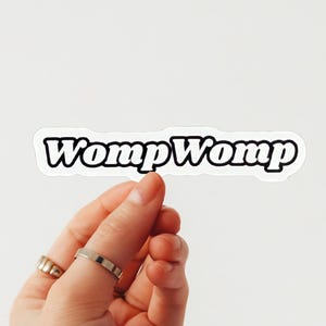 Puede incluir: Pegatina blanca con el texto "Womp Womp" en letras negras en negrita.