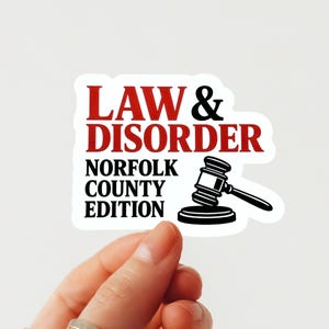 Puede incluir: Una pegatina blanca con el texto "LAW & DISORDER" en rojo y negro, con "NORFOLK COUNTY EDITION" debajo. Un gráfico en blanco y negro de un martillo está presente.
