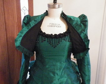 May include: A green dress with a black lace trim and beaded neckline. The dress has a fitted bodice and a full skirt. The dress is open in the front, revealing a black lining.