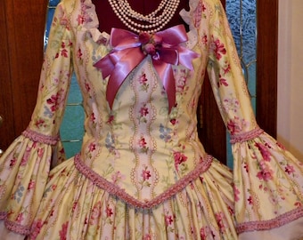 May include: A yellow and pink floral dress with a pink ribbon and pearl necklace. The dress has long sleeves with lace trim and a full skirt.