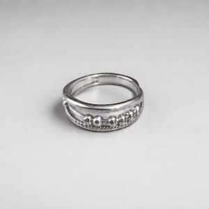 Peut inclure: Une bague argentée au design multi-anneaux. La bague se compose d'un anneau lisse, d'un anneau à la texture torsadée et d'un anneau orné d'une série de petites perles argentées polies et rondes, régulièrement espacées sur la circonférence.