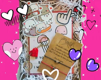 May include: A gift box filled with a variety of items, including stickers, a card, a keychain, and a friendship bracelet. The box is filled with shredded paper and has a pink background. The items are all themed around love and friendship.