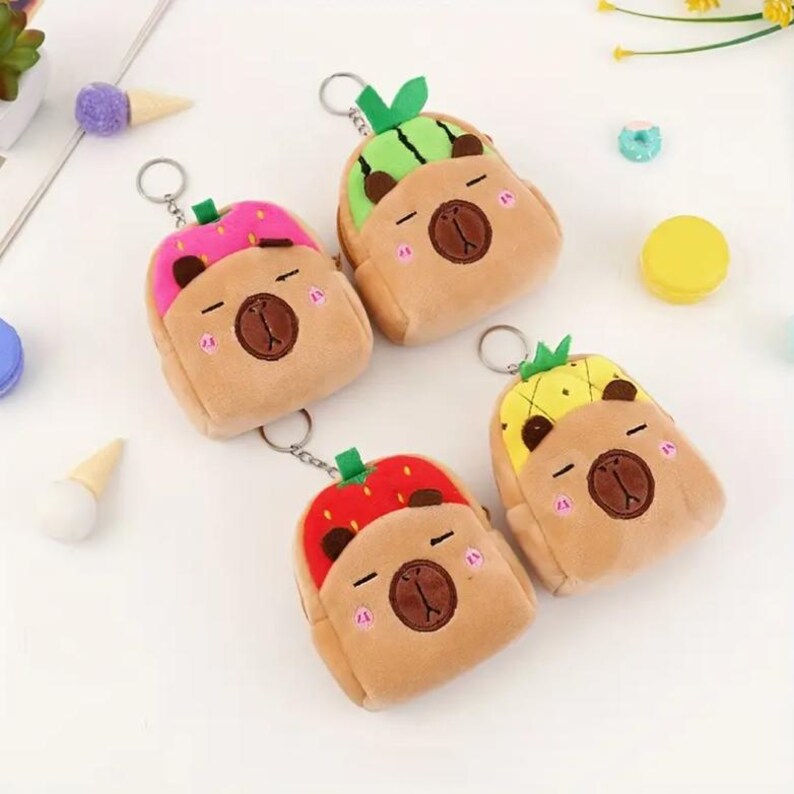 May include: Four plush keychains in the shape of a bear with fruit-themed tops. The fruits are watermelon, strawberry, pineapple, and a pink donut. Each keychain has a metal ring for attaching keys.