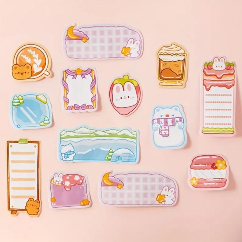 May include: A collection of colorful, die-cut stickers with various designs. The stickers feature cute illustrations of animals, food, and scenery, including a bear with coffee, a polar bear with a scarf, and a strawberry bunny. The stickers are on a pink background.