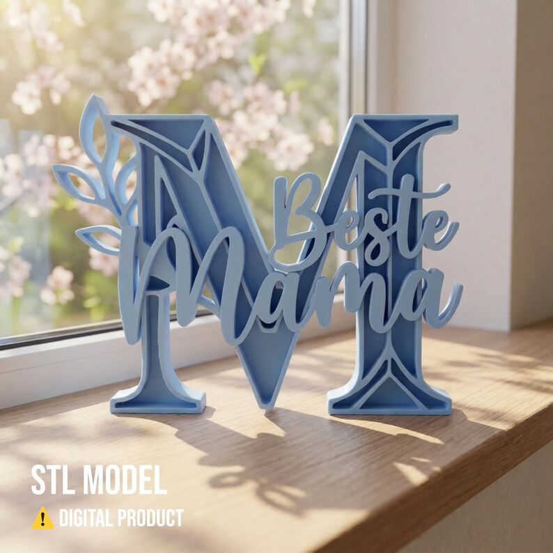 Op de afbeelding: Een lichtblauwe decoratieve letter "M" met de woorden "Beste Mama" in script. De letter heeft een bloemenontwerp aan de linkerkant en wordt weergegeven op een houten oppervlak bij een raam. De tekst "STL MODEL" en "DIGITAL PRODUCT" staan onderaan.