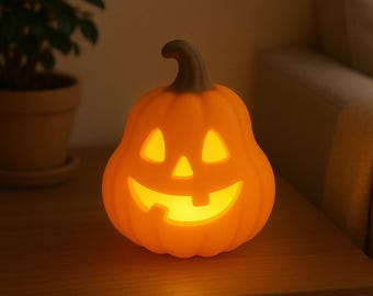 May include: An illuminated orange pumpkin-shaped Halloween decoration with a carved face. The pumpkin has a dark brown stem and is lit from within, casting a warm glow. The decoration is on a wooden surface.