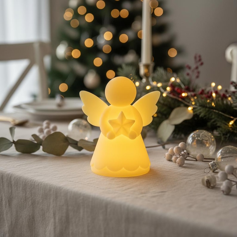 May include: A glowing angel-shaped LED light with outstretched wings and a star in its hands. The soft yellow light illuminates the angel, creating a warm, inviting ambiance. The angel is placed on a table with holiday decorations, including a Christmas tree in the background.