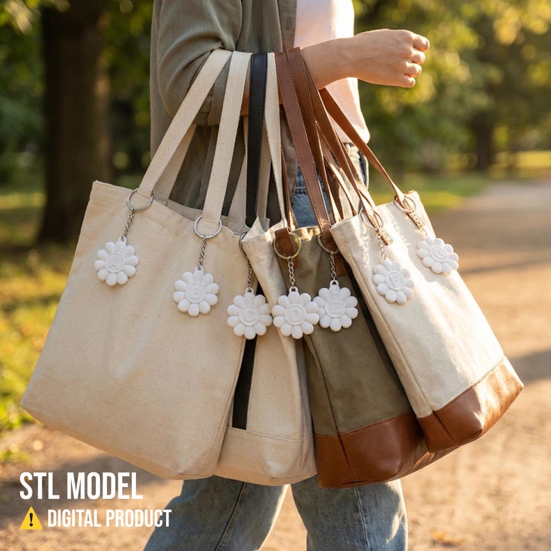 May include: Several canvas tote bags in various colors, including beige, olive green, and brown, are held by a person. Each bag has a matching strap and a white daisy-shaped charm. The bags are of different sizes and styles.