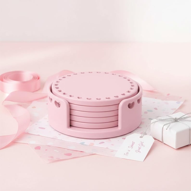 May include: A set of six pink coasters with heart-shaped cutouts, stacked in a matching holder. The coasters have a decorative edge. A gift tag reads "For a Sweet Girl". Pink ribbon and a small gift box are also present.
