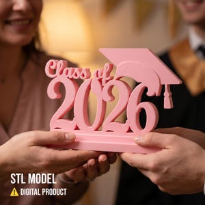 May include: A pink graduation decoration with the text "Class of 2026" and a graduation cap. The words "STL MODEL" and "A DIGITAL PRODUCT" are at the bottom. The decoration is held by two people.