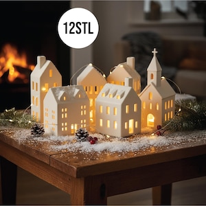 May include: A collection of cream-colored ceramic houses and a church with lit windows, arranged on a wooden table with faux snow, pinecones, and string lights. The text "12STL" is in a white circle in the upper left.